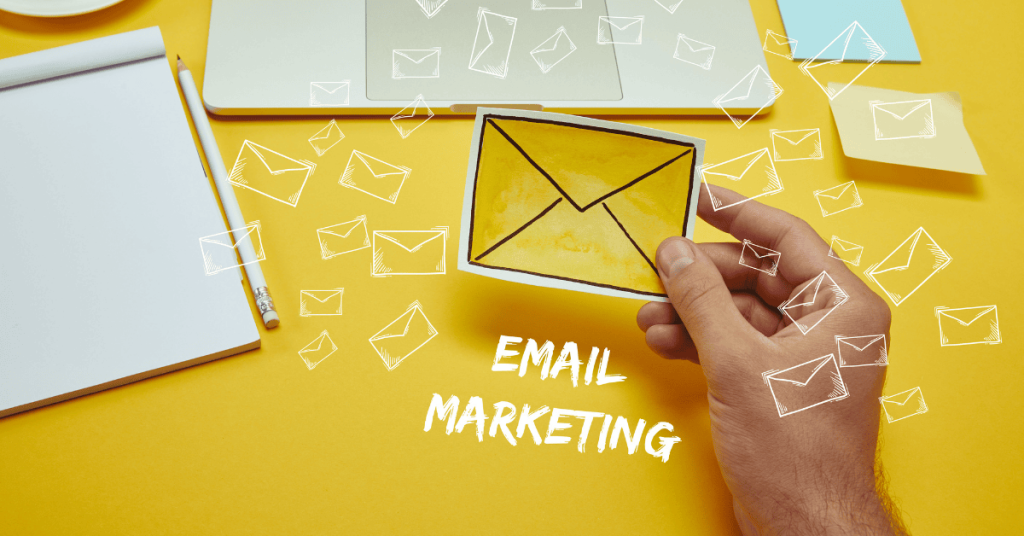 cropped image of man holding envelope sign near laptop with 'email marketing' lettering and email icons