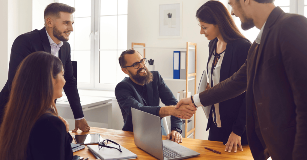 Smiling Business Partners Shaking Hands after Successful Negotiations with Colleagues in Office