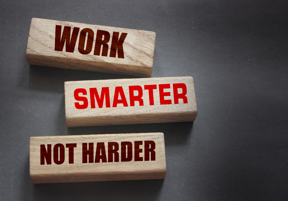 buy back your time: Three wooden blocks are stacked on a dark surface. The top block reads 'WORK' in red capital letters. The middle block reads 'SMARTER' in red capital letters. The bottom block reads 'NOT HARDER' in red capital letters.